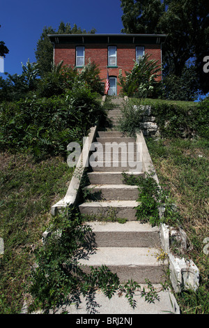 Una casa in mattoni rossi sulla cima di una collina, con una scala di cemento che conduce e bandiera americana nei pressi di porta. Foto Stock