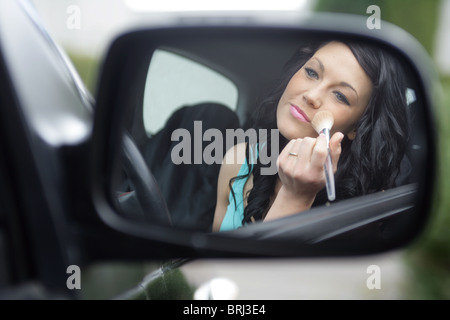 Dai capelli scuri donna di applicare il make up nel suo specchietto laterale. Foto Stock