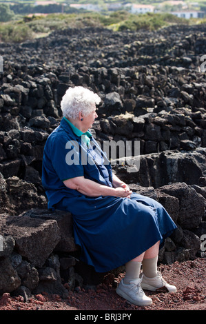 Donna anziana seduta su un muro di lava, Madalena, Pico, Azzorre, Portogallo. Foto Stock