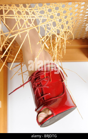 La donna è la gamba in piedi su una sedia rotta con la gamba attraverso la rotta sezione del sedile Foto Stock