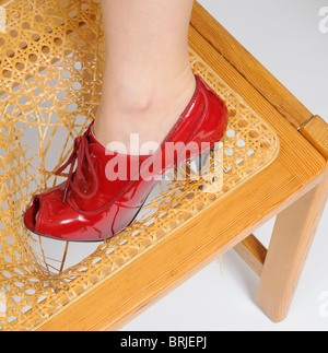 La donna è la gamba in piedi su una sedia rotta con la gamba attraverso la rotta sezione del sedile Foto Stock