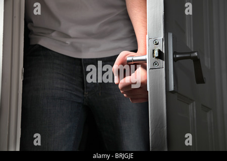 Maschio lato ruotando la maniglia di una porta di entrare in una stanza buia Foto Stock