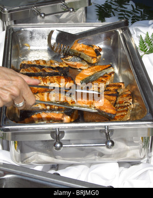 Appena cucinata e deliziosi salmone bistecche servite da acciaio inossidabile server di riscaldamento su una lussuosa nave da crociera. Servire tong Foto Stock