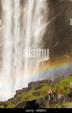 Una giovane donna esplora al di sotto di una cascata gigantesca. Foto Stock