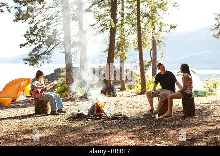 I giovani adulti camping sedersi attorno a un fuoco accanto a un lago in Idaho. Foto Stock