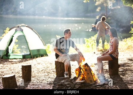 I giovani adulti camping sedersi attorno a un fuoco accanto a un lago in Idaho. Foto Stock