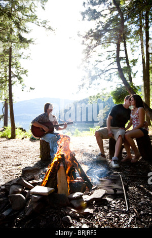 I giovani adulti camping sedersi attorno a un fuoco accanto a un lago in Idaho. Foto Stock