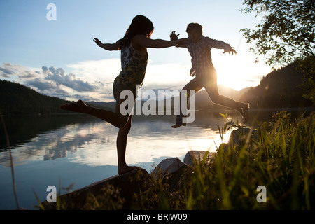 Due giovani adulti in equilibrio su rocce al tramonto accanto al lago. Foto Stock