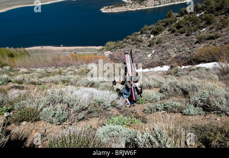 Un giovane uomo cambia il suo scarponi da telemark per scarpe per l'ultima parte del sentiero, durante una molla sci tour nel giugno del lago, Calif Foto Stock