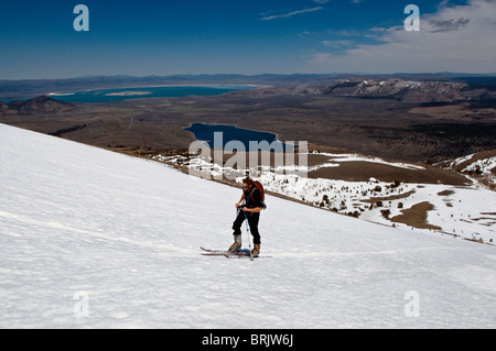 Durante il suo ultimo tour di sci per la stagione, un giovane uomo di pelli fino alla montagna con Mono Lago sullo sfondo, in giugno Lago, Calif Foto Stock