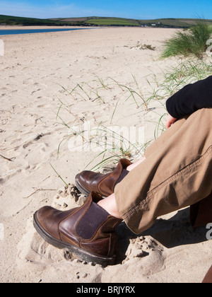 Senior donna seduta sulla spiaggia di roccia, Cornwall, Inghilterra. Foto Stock