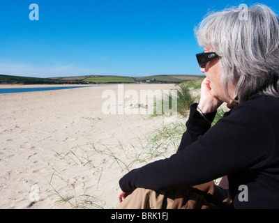 Senior donna seduta sulla spiaggia di roccia, Cornwall, Inghilterra. Foto Stock