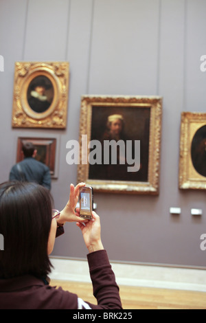Femmina turista giapponese di fare una foto con il suo telefono cellulare del famoso autoritratto di Rembrand al Louvre di Parigi Foto Stock