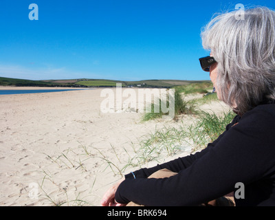 Senior donna seduta sulla spiaggia di roccia, Cornwall, Inghilterra. Foto Stock