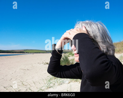 Donna anziana seduta sulla spiaggia di Rock, Cornovaglia, Inghilterra. Foto Stock