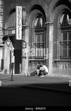 Due uomini seduti sul marciapiede in Parigi vicino all'ingresso della sala di emergenza in bianco e nero Foto Stock