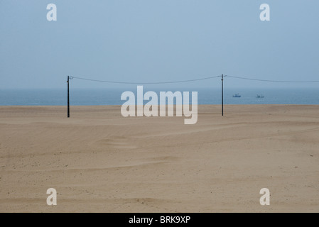 I pali dell'elettricità a Figueira da Foz Beach con un paio di barche in mare in un giorno nuvoloso, Portogallo Foto Stock