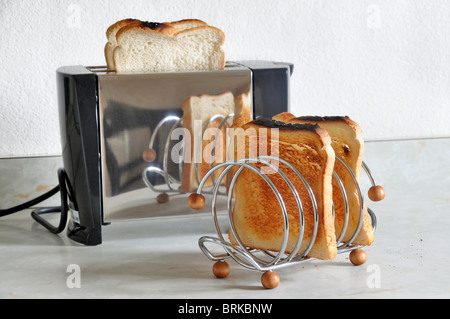 Il pane in un acciaio inossidabile tostapane con un toast rack con fette di pane tostato seduto davanti. Foto Stock