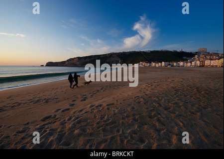 Un giovane e il loro cane a camminare sulla spiaggia al tramonto a Nazaré, Portogallo Foto Stock