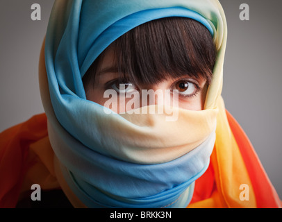 Bruna ragazza in testa multicolore sciarpa; fotografato su sfondo grigio Foto Stock