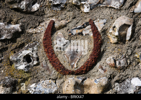 Horsehoe incorporato nel vecchio muro di pietra focaia per fortuna. Charlton village, West Sussex. Foto Stock