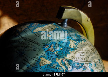 Un piccolo globo vintage della Terra, evidenziando l'Emisfero Settentrionale e in Europa, con un'antica mappa come sfondo. Foto Stock