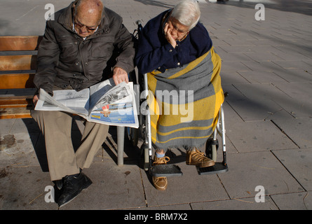 Spagna Barcellona, vecchia coppia senior seduta sul banco in sun, leggendo il giornale e dormire Foto Stock