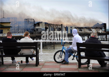 La gente guarda Hastings Pier dopo un incendio doloso nelle prime ore di questa mattina lo lascia quasi completamente distrutta Foto Stock