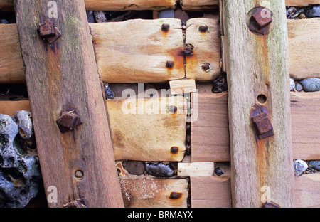 Dettaglio di weathered costiere groyne legname con bulloni gigante e ciottoli costretti dalle onde in fessure tra assi Foto Stock