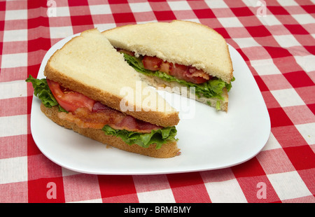 Uno completato e fette di pancetta, lattuga e pomodoro blt su una piastra bianca sulla tovaglia tradizionale Foto Stock