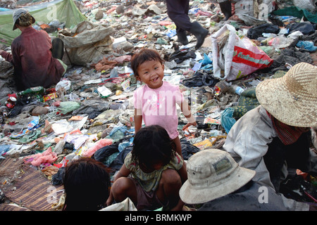 Una giovane ragazza che vivono in condizioni di povertà è sorridente come la sua famiglia è la cernita di rifiuti riciclabili in una discarica di rifiuti in Phnom Penh Cambogia. Foto Stock