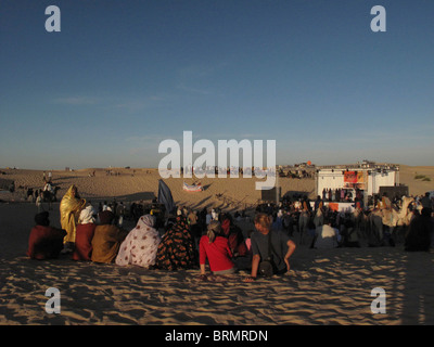 I turisti al Festival di musica nel deserto seduti sulla sabbia a guardare una performance Foto Stock