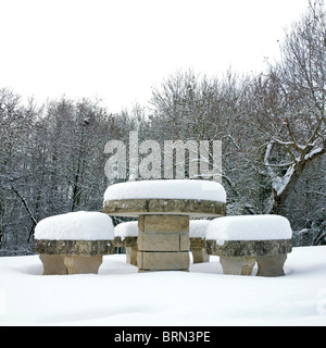 Tavolo e panchine in pietra ricoperti di neve in un paesaggio invernale circondato da alberi Foto Stock
