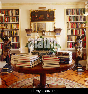 Libri in cumuli di circolare su tavolo antico in biblioteca sala da pranzo con finestre da pavimento a soffitto e scaffali blackamoor statue Foto Stock