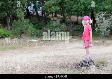 Foto di stock di un 4 anno vecchia ragazza in piedi su un ceppo di albero. Foto Stock