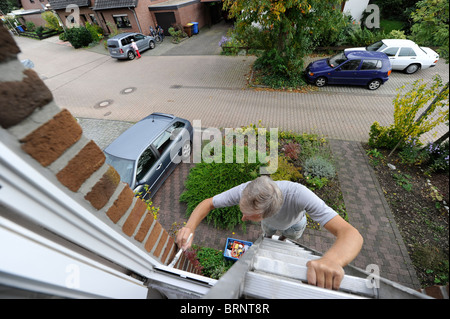 L'uomo pittura la sua casa da una scaletta. Foto Stock