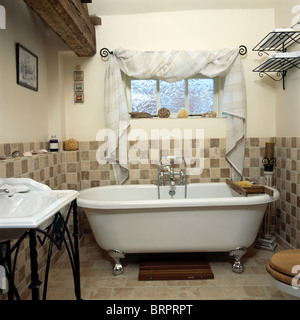 Roll-top vasca sottostante finestra drappeggiati con tessuto bianco in pole nel paese bagno con dado-Altezza pareti piastrellate Foto Stock
