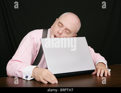 Uomo d'affari che dorme sul lavoro mentre si lavora al suo computer portatile sul nero Foto Stock
