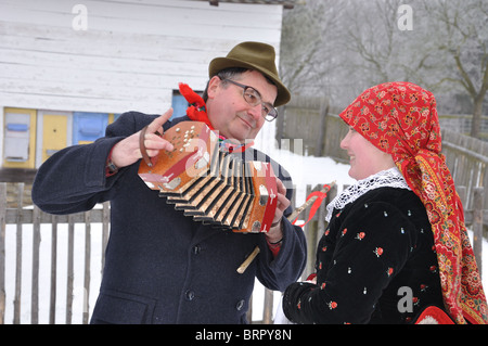 L'uomo gioca sulla fisarmonica per la ragazza in costumi folk in inverno al tempo di Natale Foto Stock