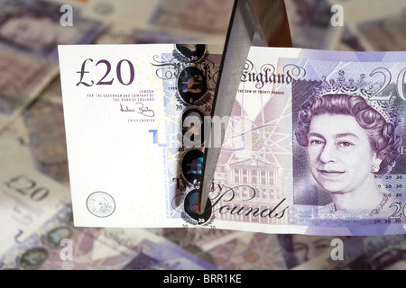 Pila di venti sterline per banconote con venti pound nota essendo tagliato con un paio di forbici nel Regno Unito Foto Stock