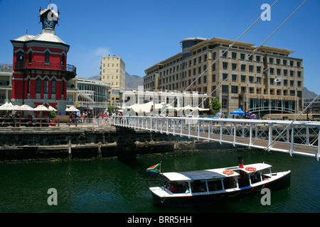 Victoria and Alfred Waterfront con la torre dell Orologio e una imbarcazione turistica passando sotto un ponte Foto Stock