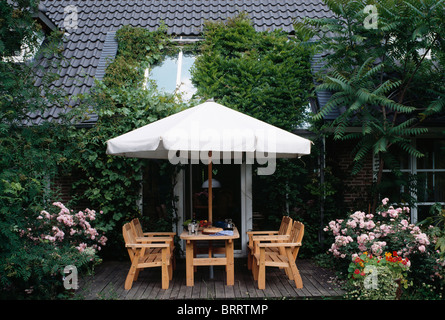 Grande ombrellone bianco al di sopra di tavoli e sedie in legno su adorna townhouse patio con le rose rosa in vasi Foto Stock