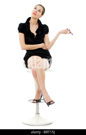 Elegante giovane donna seduta su uno sgabello in possesso di un telefono cellulare Foto Stock