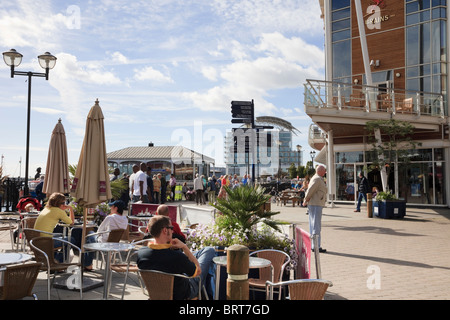 Le persone al di fuori seduta in caffetterie sul lungomare. Il Mermaid Quay, Cardiff Bay, Glamorgan, South Wales, Regno Unito Foto Stock