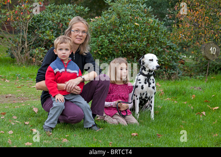 Una madre e i suoi due figli piccoli e il cane di famiglia seduti in un prato Foto Stock