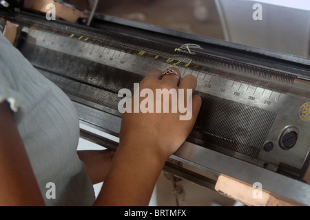 Una giovane donna Khmer è usando le mani con precisione durante il lavoro presso la sua macchina in una fabbrica di indumento in Cambogia Foto Stock