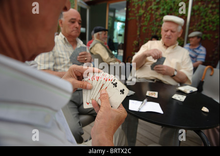 Gli uomini anziani carte da gioco all'aperto in un caffè con terrazza Foto Stock