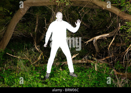 Floating alien uomo in bianco luminoso con vestiti catturati in una fitta foresta infestata da erbacce Foto Stock