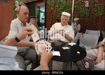 Gli uomini anziani carte da gioco all'aperto in un caffè con terrazza Foto Stock