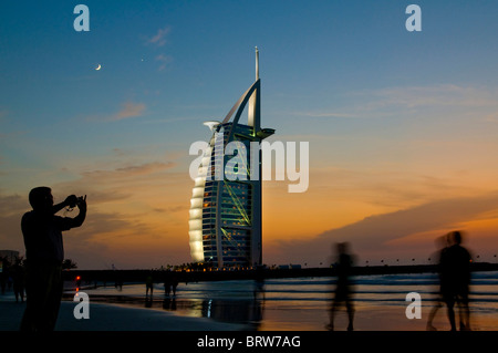 La gente sulla spiaggia di fronte all'hotel di lusso Burj al-Arab al tramonto, Dubai, Emirati Arabi Uniti Foto Stock